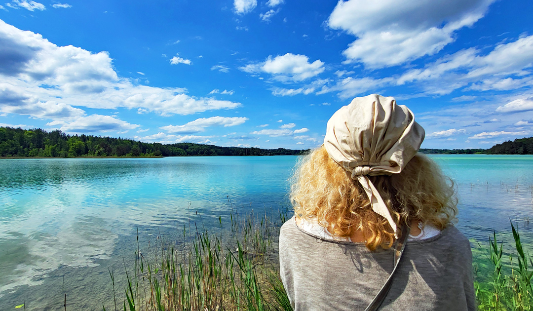 Titelbild zum Artikel "Lass los, was Du nicht beeinflussen kannst" – Frau blickt auf einen idyllischen See