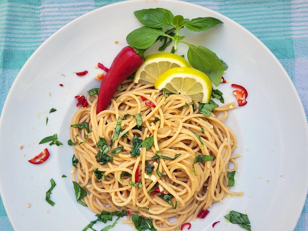 Vegane Spaghetti al Limone auf einem weißen Teller, garniert mit Zitronenscheiben, Basilikum und einer roter Chilischote.