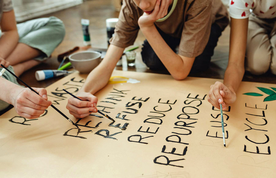 Kinder gestalten ein Plakat mit Less-Waste-Begriffen wie "Refuse", "Reduce", "Reuse" und "Recycle".