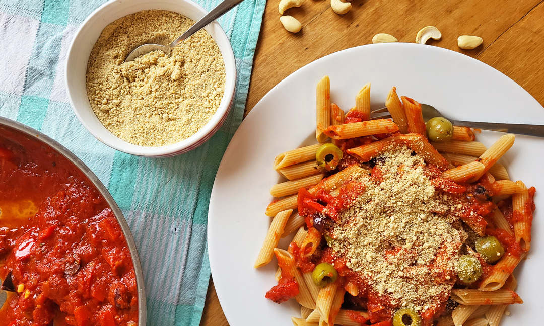 Penne alla puttanesca mit veganem Parmesan aus Cashews, Mandeln und Hefeflocken.