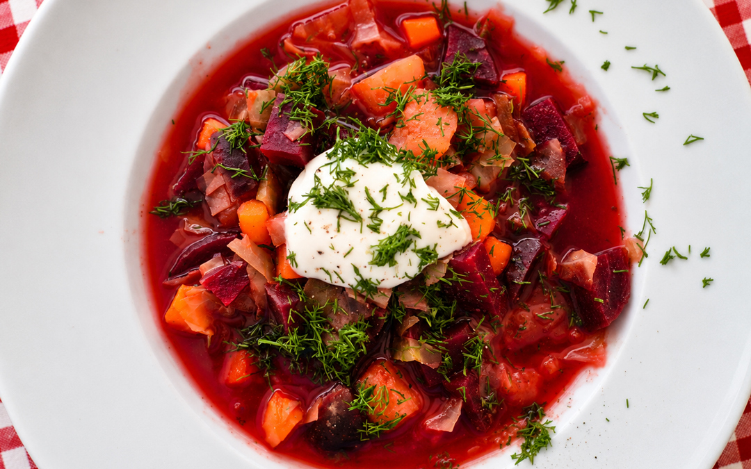Veganer Borschtsch aus Roter Bete, Spitzkohl, Kartoffeln und Karotten mit Sojajoghurt und frischem Dill in einem weißen Suppenteller